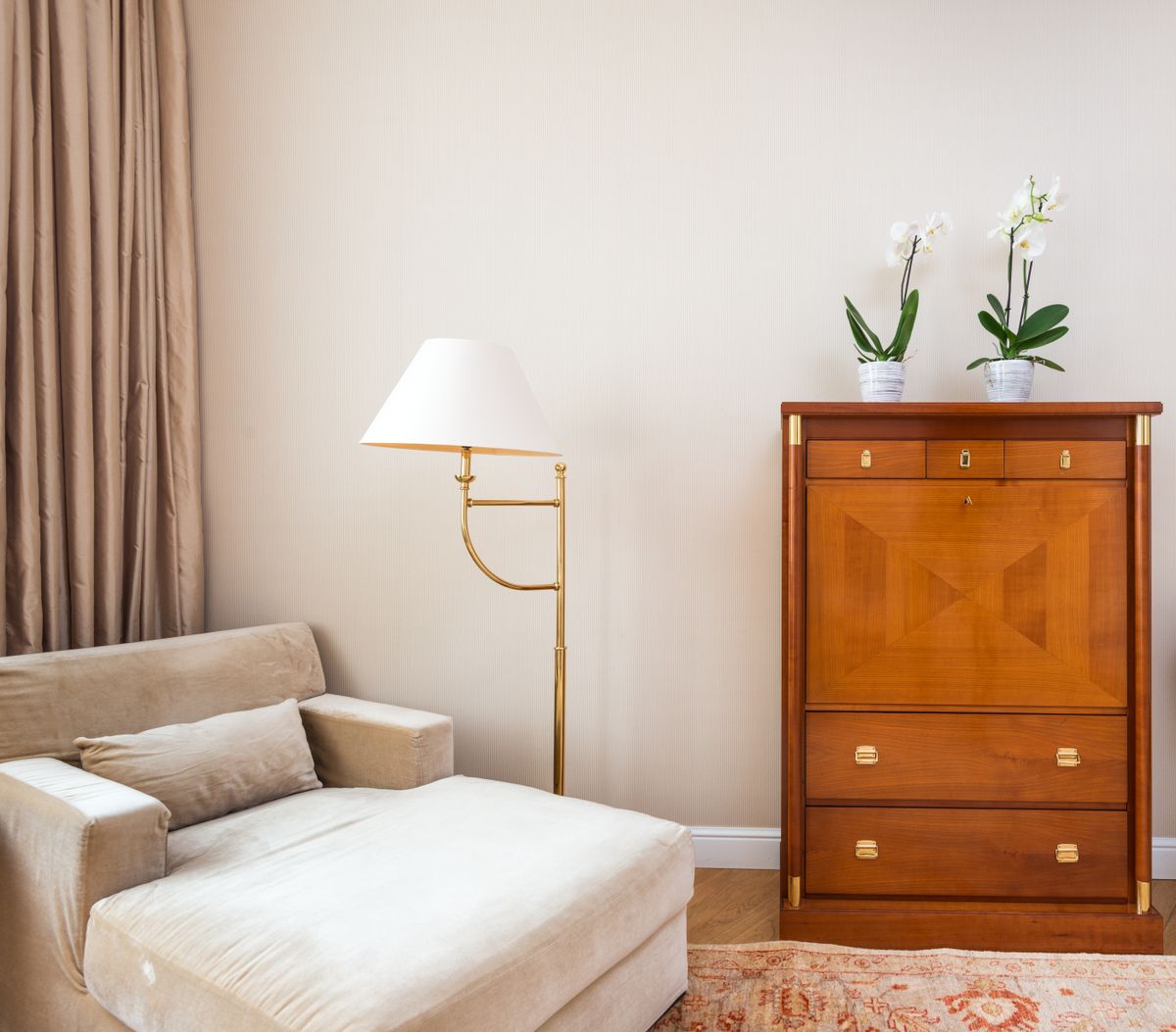 Warmer Sitzbereich mit Sessel, Messinglampe und Orchideen auf einer Holzkommode